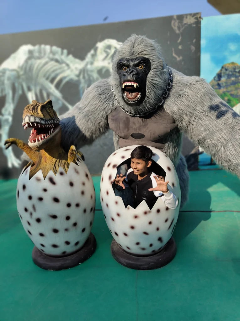 A boy peeks out of a dinosaur egg next to a large gorilla statue.