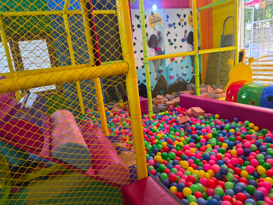 A colorful indoor playground with a ball pit and climbing wall, filled with children playing.