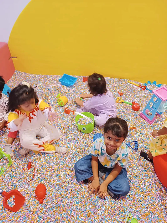 Young children play in a ball pit filled with colorful balls and toys.