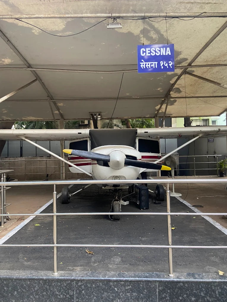 A small white airplane with a propeller is displayed under a covered area, with a sign reading "CESSNA" in English and Marathi.