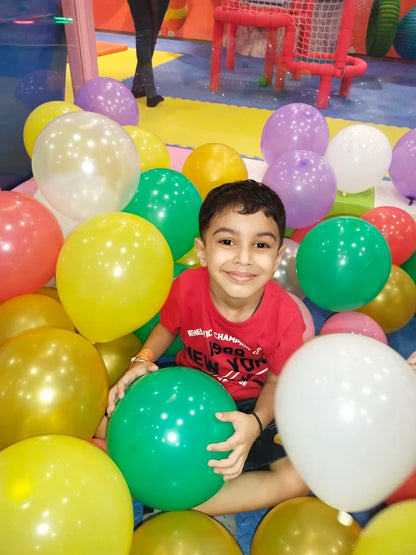 A young boy smiles surrounded by colorful balloons in a play area.