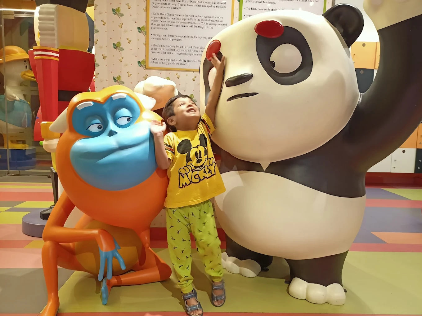 A young child plays with a large panda statue, next to a colorful monkey statue.