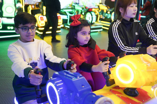 Children play an arcade racing game with bright lights and colorful machines.