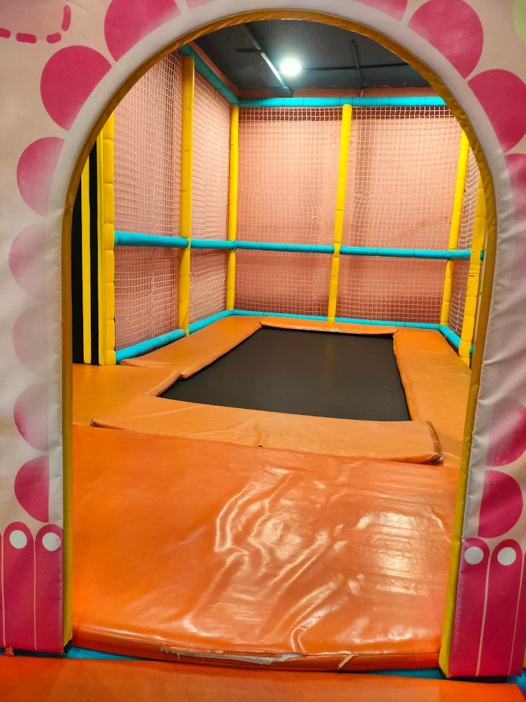 An indoor trampoline area with orange padding and safety netting, viewed through a colorful archway.