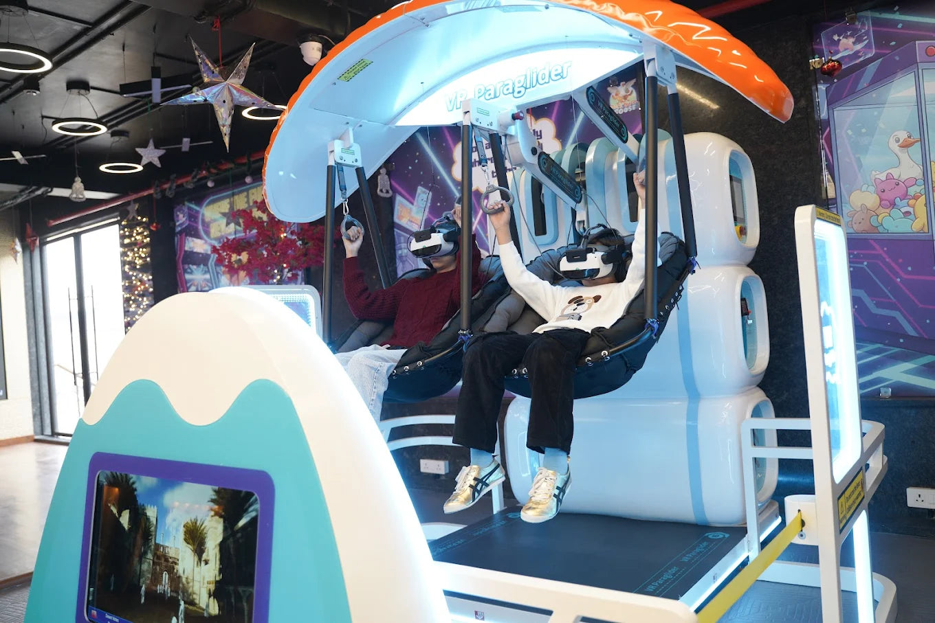 Two young people experience a VR paraglider ride, wearing headsets and holding onto handles.