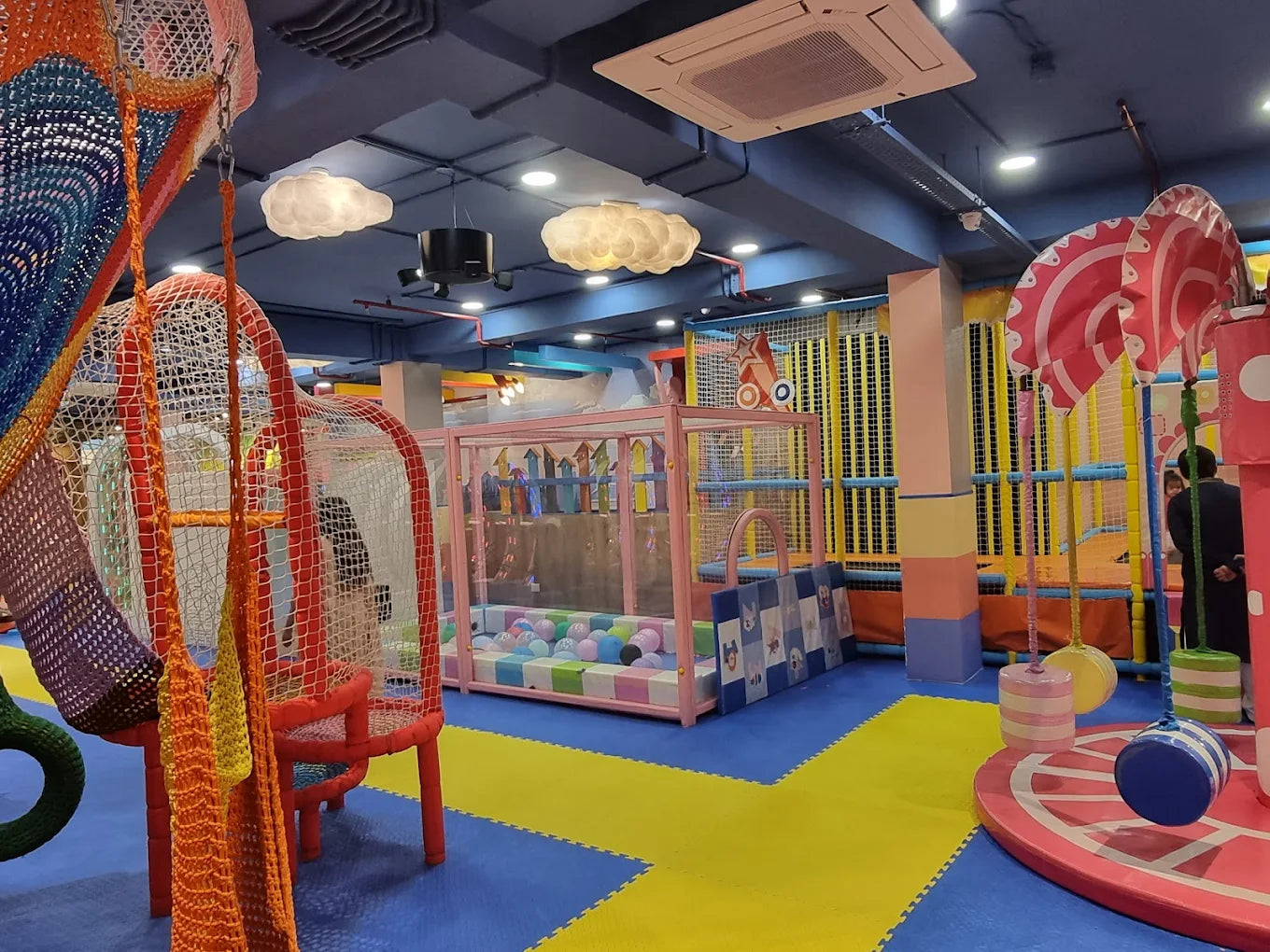 A colorful indoor playground with soft play structures and a ball pit, featuring children playing.
