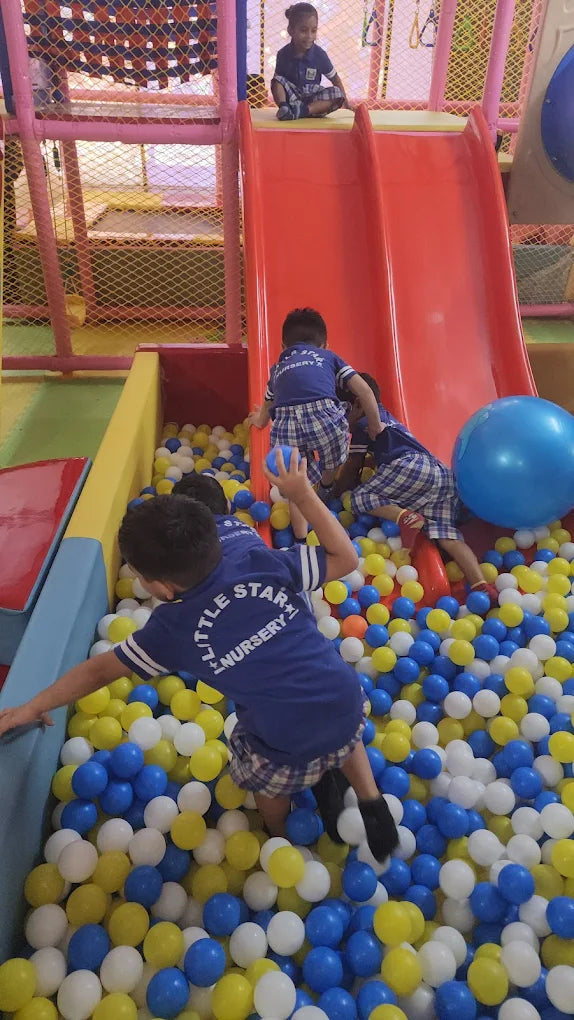Children play in a ball pit and on a slide at an indoor playground.