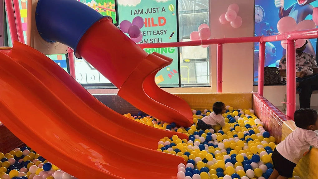 Toddlers play in a ball pit with slides at a children's play area.