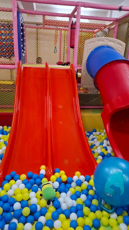 A colorful indoor playground with slides and a ball pit, featuring a stuffed toy.