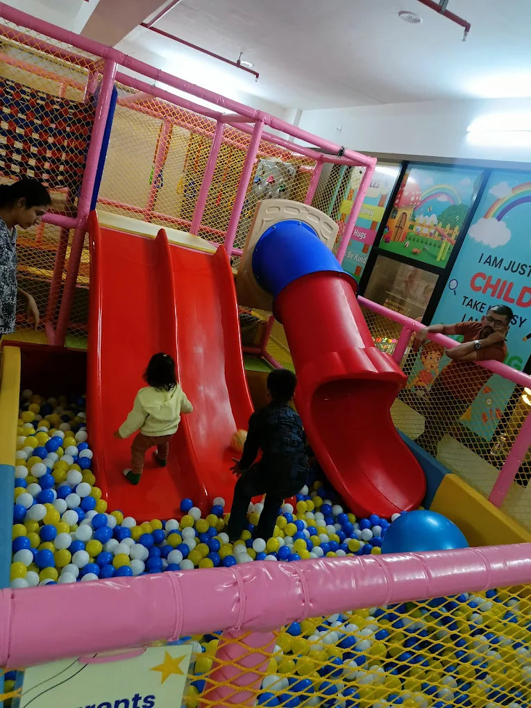 Children play in a ball pit with slides at an indoor playground.