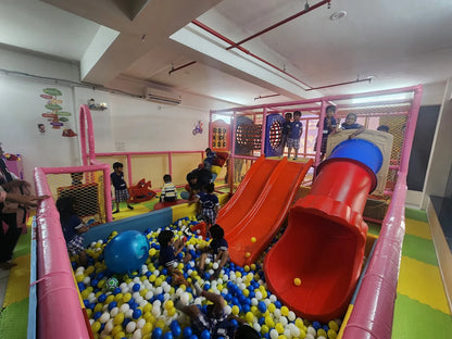 Children play in a colorful indoor playground with slides and a ball pit.
