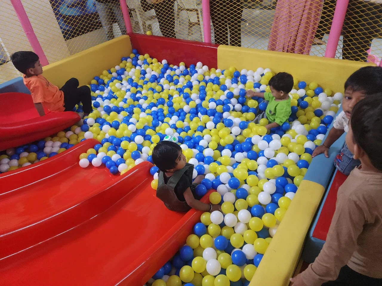 Children play in a ball pit with red slides.