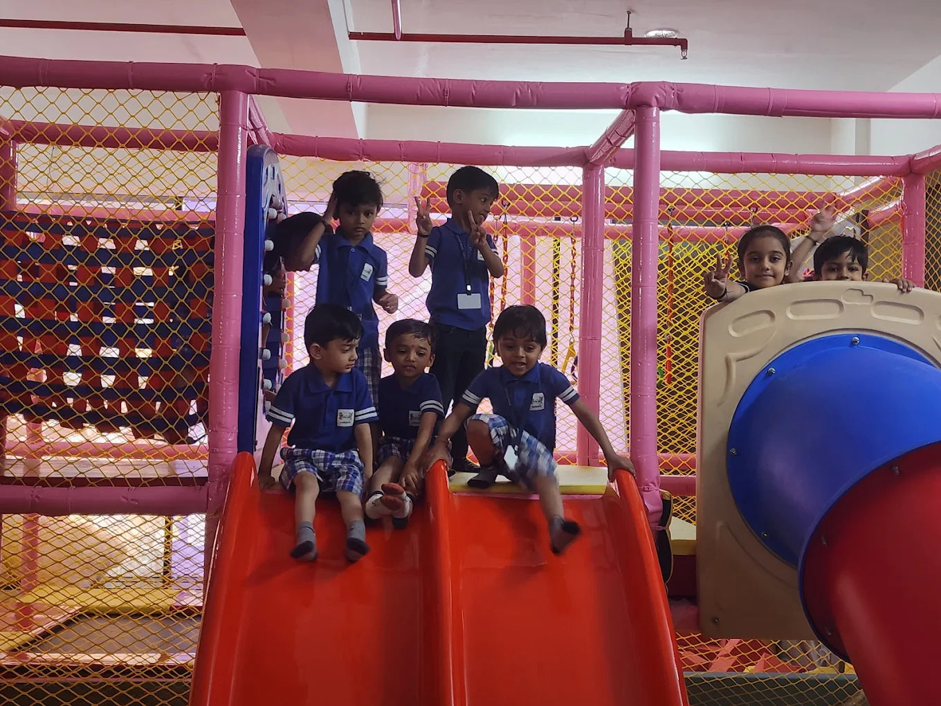 Children play on a red slide in a colorful indoor playground.