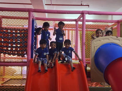 Children play on a red slide in a colorful indoor playground.