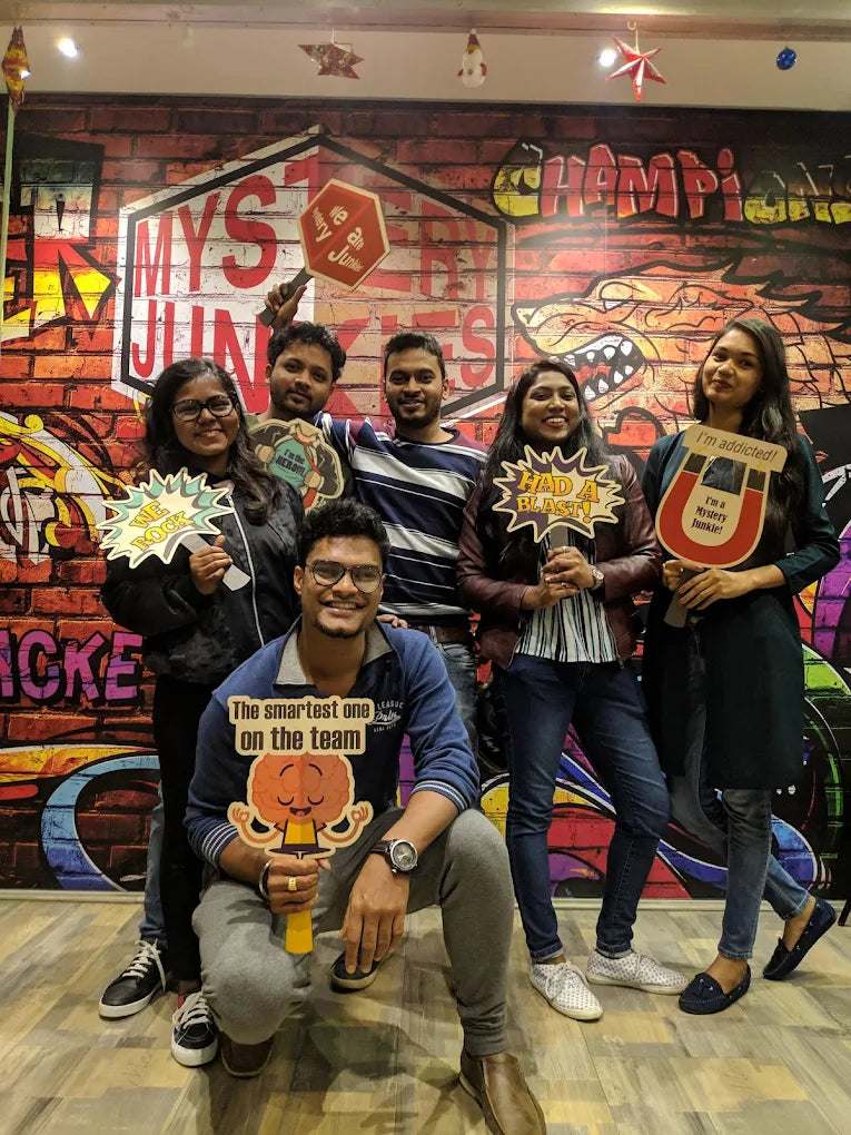 A group of young adults poses for a photo in front of a graffiti-style wall, holding fun signs.