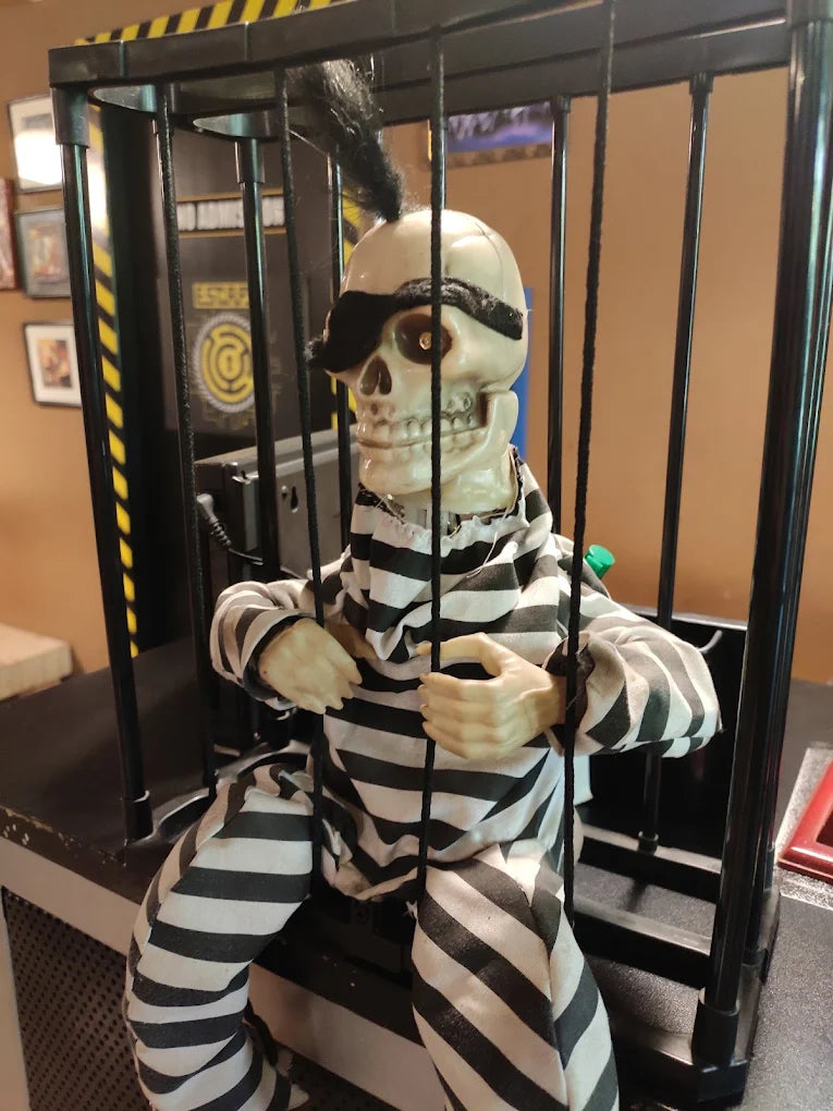 A skeleton in a prisoner costume sits in a cage.