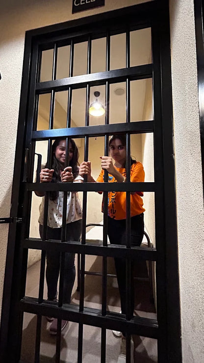Two young women playfully pose behind the bars of a jail cell.
