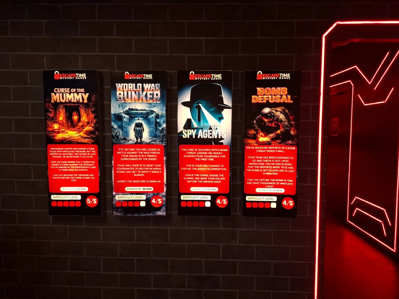Four escape room posters with themes of a mummy's curse, a World War II bunker, spy agents, and bomb defusal, displayed on a brick wall.