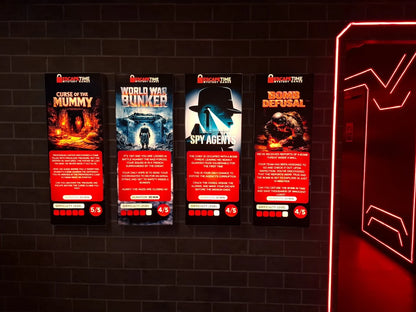 Four escape room posters with themes of a mummy's curse, a World War II bunker, spy agents, and bomb defusal, displayed on a brick wall.