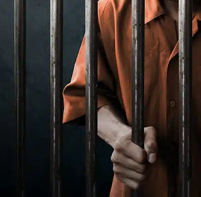 A person in an orange jumpsuit grips prison bars.