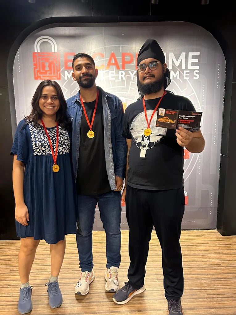 Three young adults pose with medals and coupons in front of an escape room backdrop.