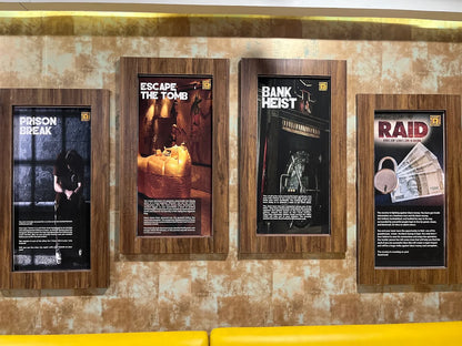 Four framed posters on a wall advertise escape room games: Prison Break, Escape the Tomb, Bank Heist, and Raid.
