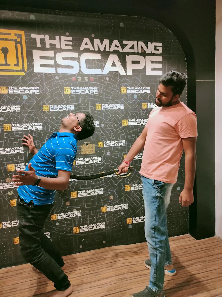 Two young men playfully pose with a prop sword in front of a "The Amazing Escape" backdrop.
