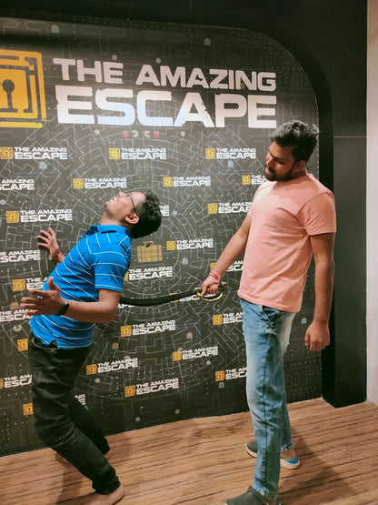 Two young men playfully pose with a prop sword in front of a "The Amazing Escape" backdrop.