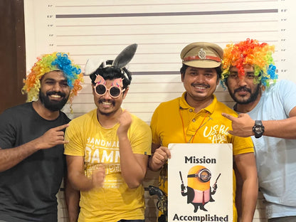 Four young men in colorful wigs and costumes pose for a photo in front of a height chart, holding a sign with a minion.