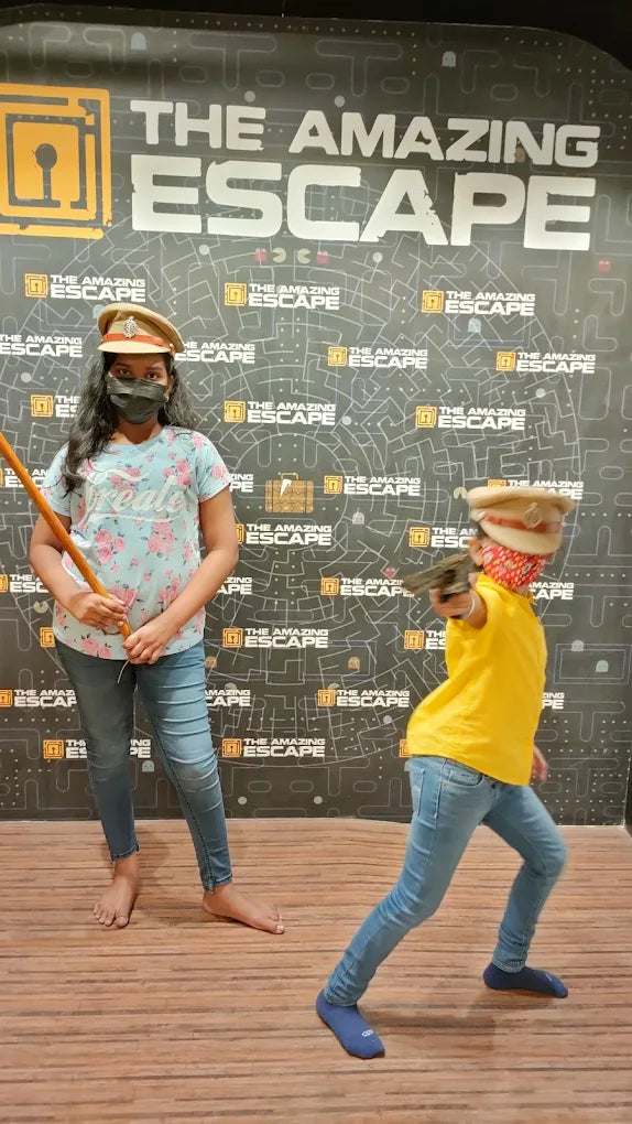 Two children in police costumes pose with props in front of a "The Amazing Escape" backdrop.