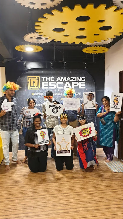 A group of young adults poses for a photo in front of "The Amazing Escape" logo, holding props and signs.