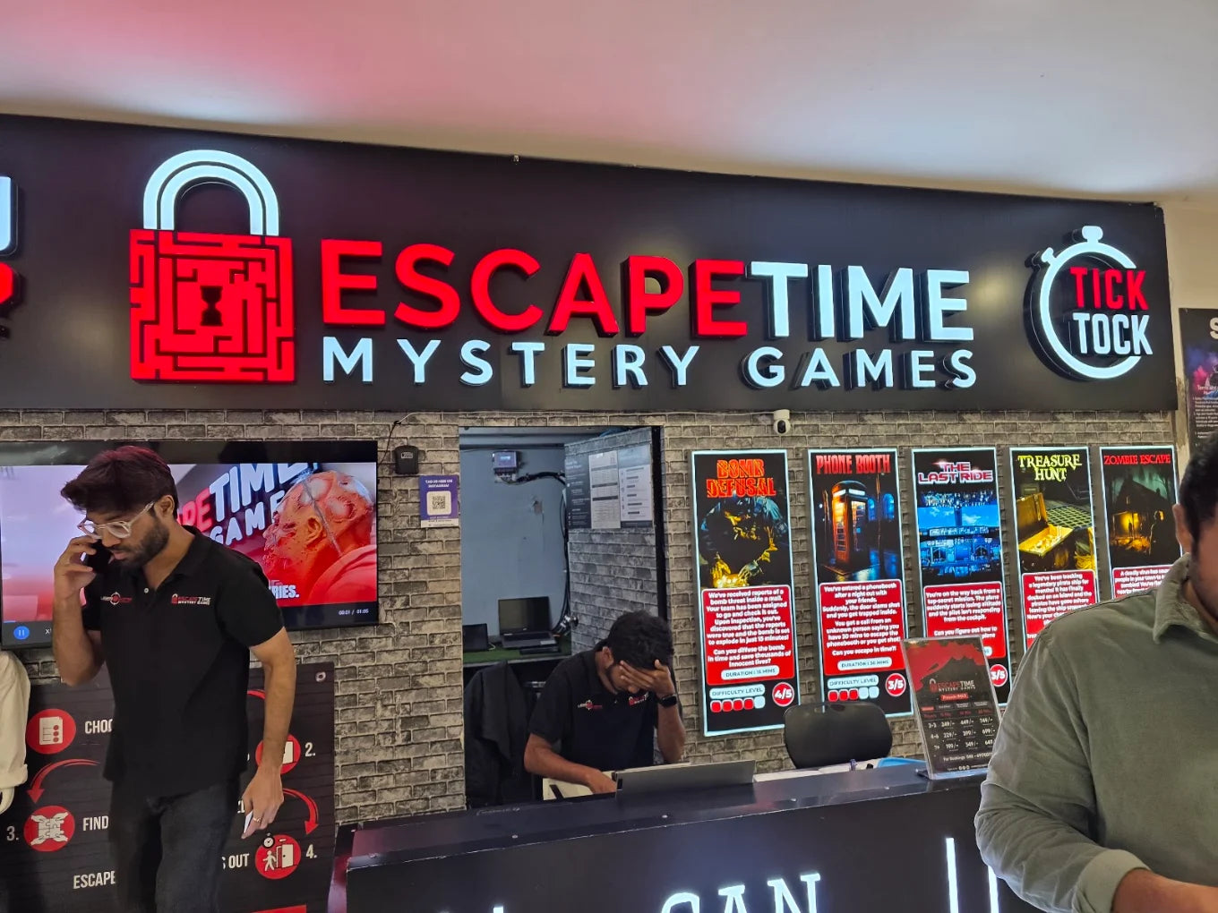 Escape room entrance with neon sign and posters of games. Young men are visible.