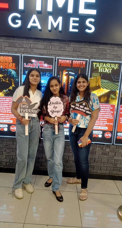 Three young women pose with signs in front of "Time Games" posters.