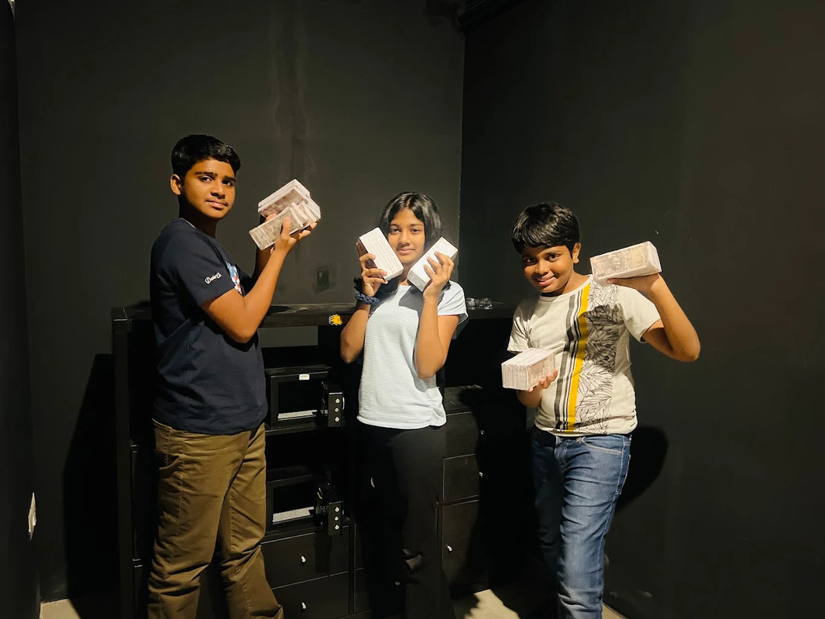 Three children hold stacks of what appear to be money in a dark room.