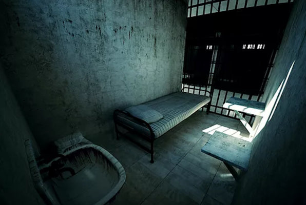 A stark prison cell with a cot, sink, and barred door, illuminated by a single beam of light.