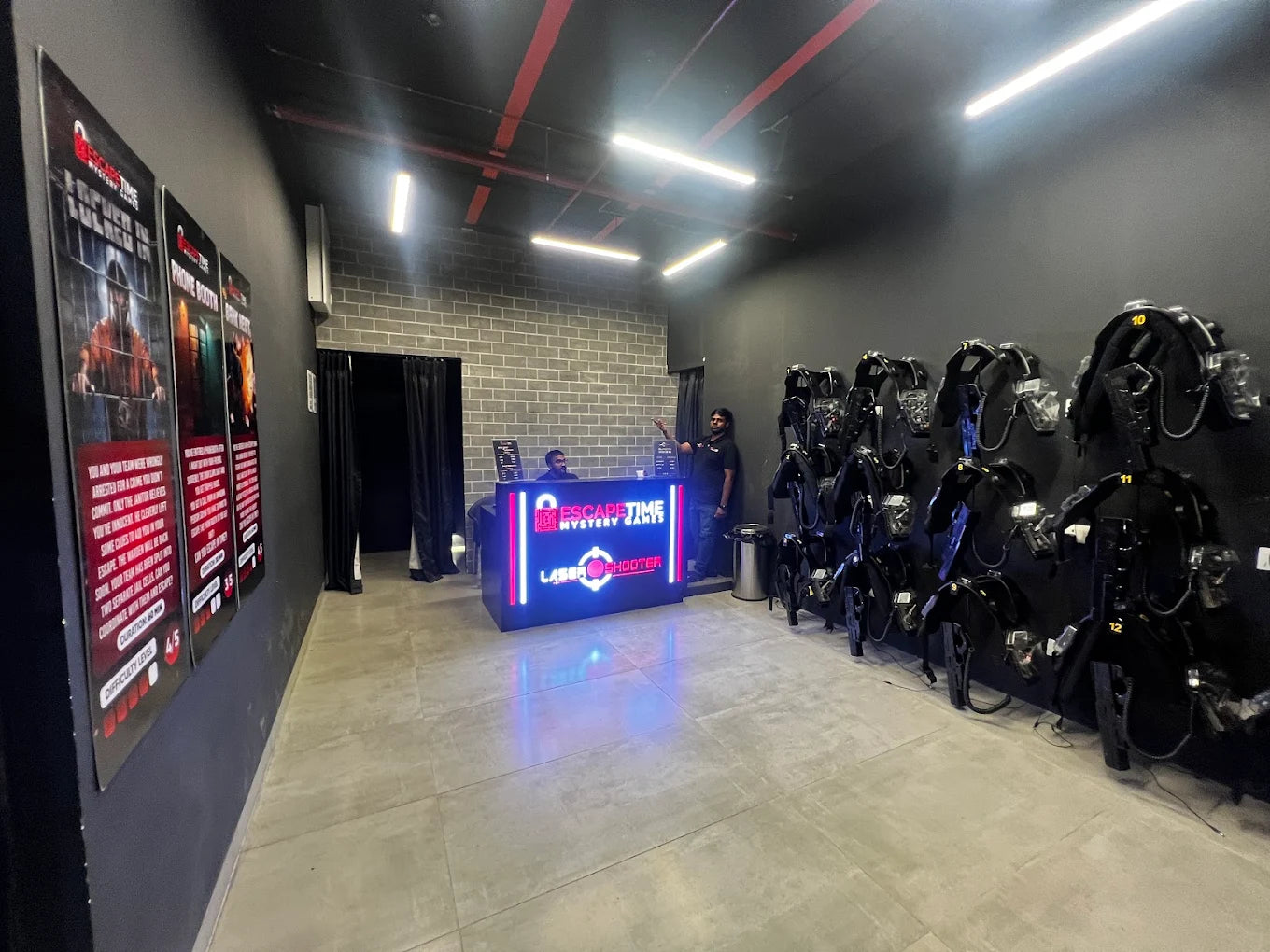 Laser tag vests hang on a wall in a dimly lit entertainment venue with a reception desk.