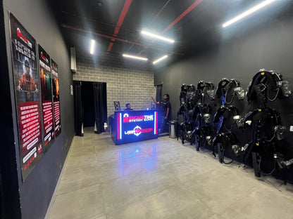 Laser tag vests hang on a wall in a dimly lit entertainment venue with a reception desk.