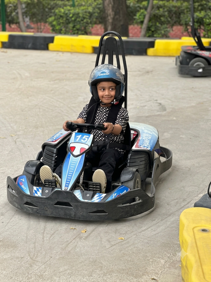 A young child wearing a helmet drives a go-kart on a track.