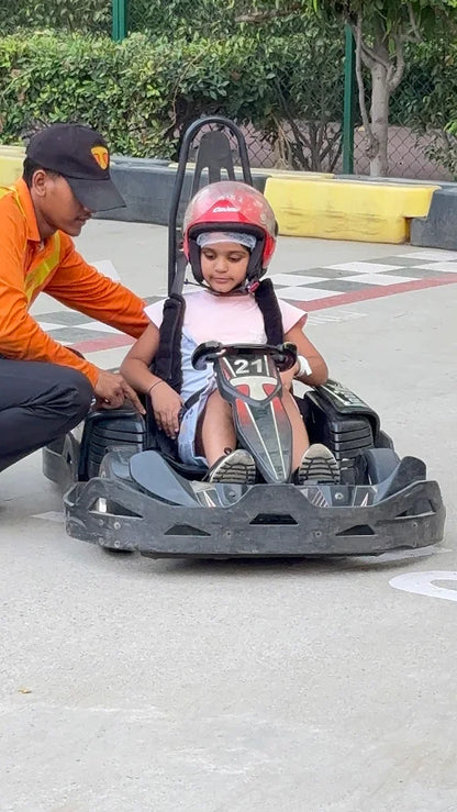 A child in a go-kart helmet is being helped by an adult at a track.