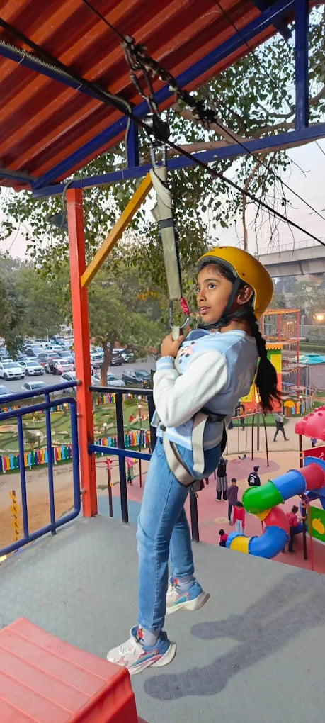 A young girl in a yellow helmet ziplines at an outdoor adventure park.