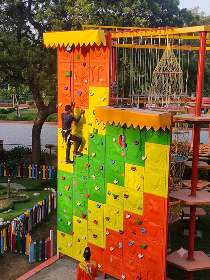 A young person climbs a colorful rock wall at an outdoor adventure park.
