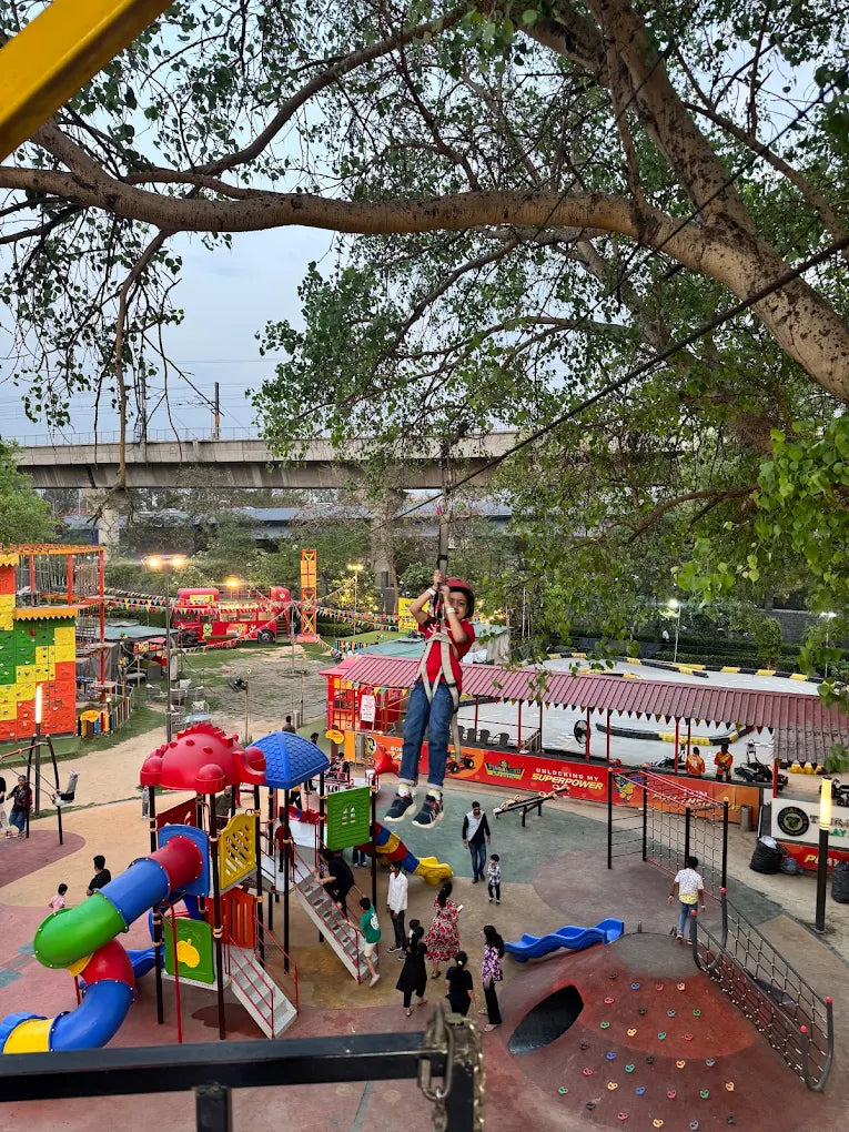 A child on a zipline at an outdoor adventure park with playgrounds and go-karts.