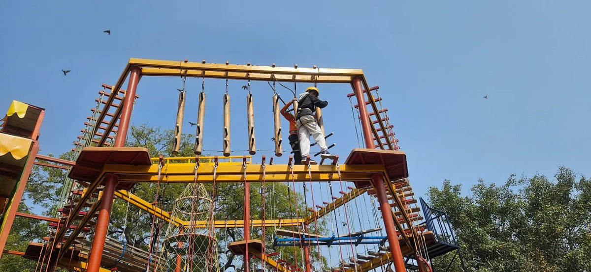 Two people on an adventure course with wooden obstacles and rope bridges against a clear blue sky.