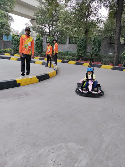 A child drives a go-kart while adults stand nearby on a track.