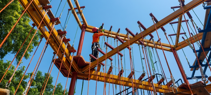 A child in a helmet and safety harness navigates an aerial adventure course.