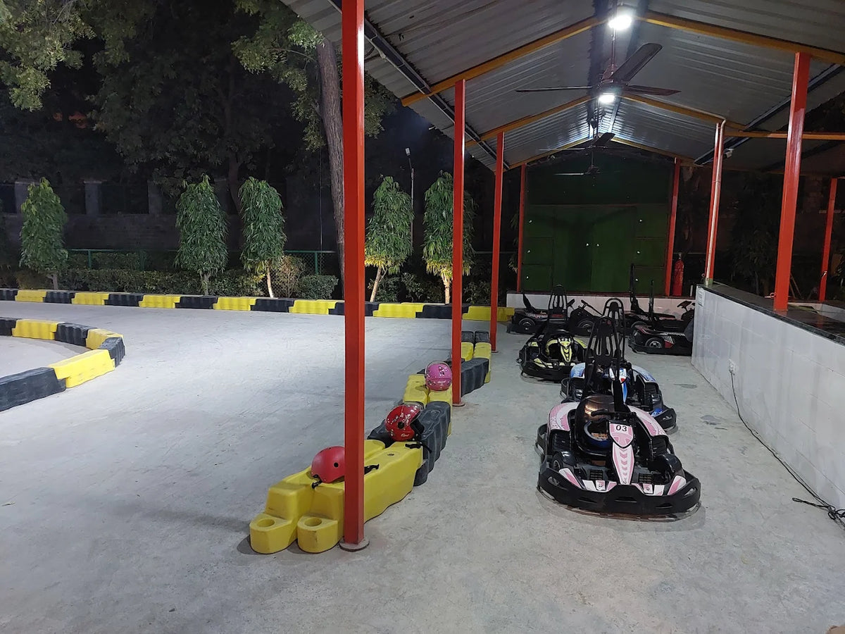 Go-karts lined up under a covered track at night, with helmets on the side.