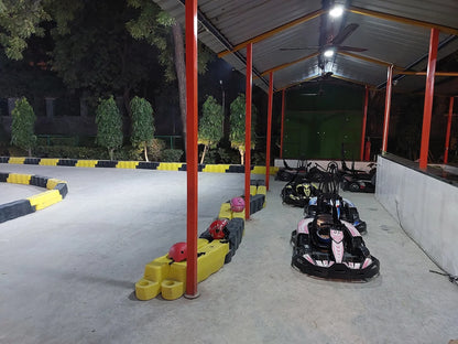Go-karts lined up under a covered track at night, with helmets on the side.