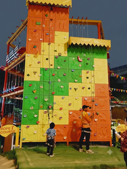 Children and an instructor at a colorful outdoor climbing wall.