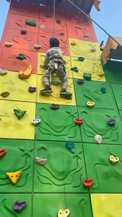 A child in a harness climbs a colorful indoor rock wall.