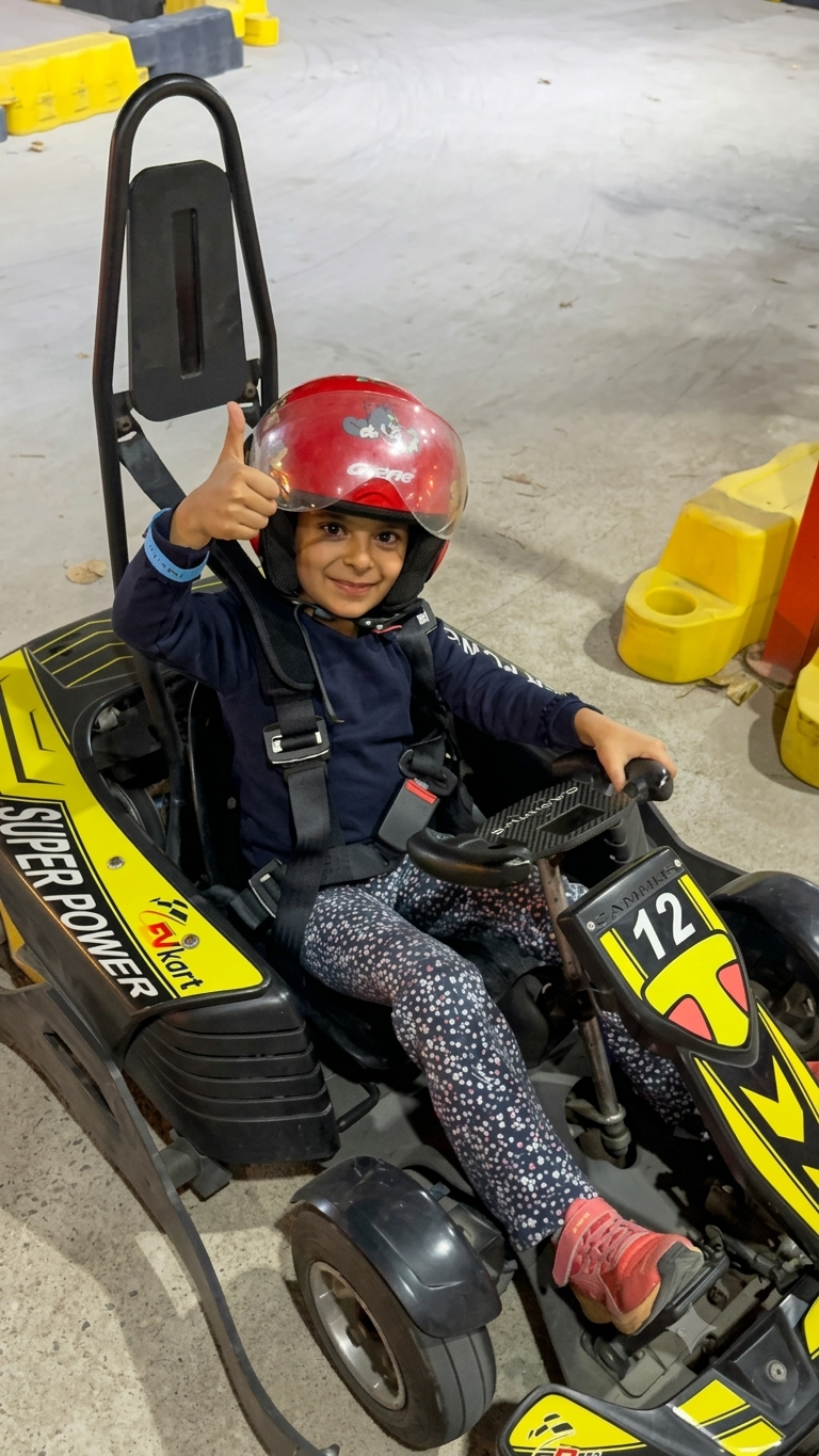 A young child in a red helmet gives a thumbs-up while sitting in a go-kart.